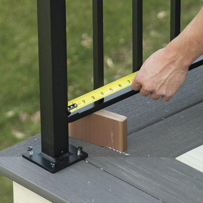 10. Position the balustrade. Slip the section into the post brackets from underneath. Use a scrap of decking to hold the balustrade snugged up into the brackets. Measure and slide the balustrade until you have it centered between the posts.